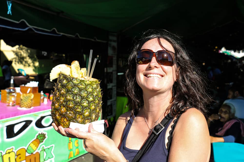 Smiling woman holding a pineapple with a straw sticking out.