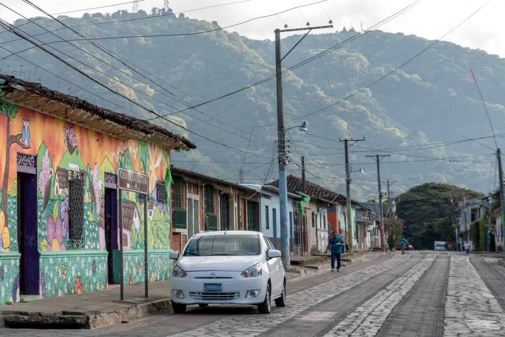 White car on a cobbled street beside a building painted in a colourful mural.